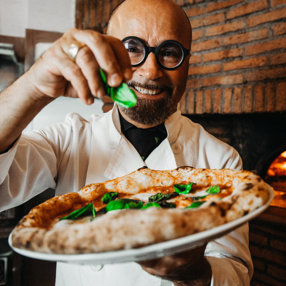 Luigi Barbaro streut frisches Basilikum auf eine Pizza